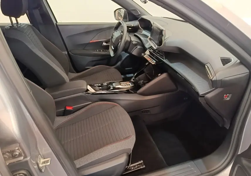 Vue intérieure côté conducteur du Peugeot E-2008 électrique gris clair, avec tableau de bord moderne et sièges tissu noirs.