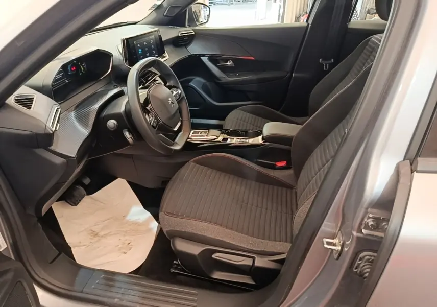 Vue intérieure côté conducteur du Peugeot E-2008 électrique gris clair 2023, avec volant cuir multifonctions et tableau de bord numérique.