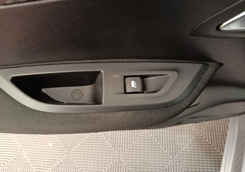 Gros plan sur la commande de lève-vitre côté porte intérieure d’une Peugeot E-2008 électrique gris clair.