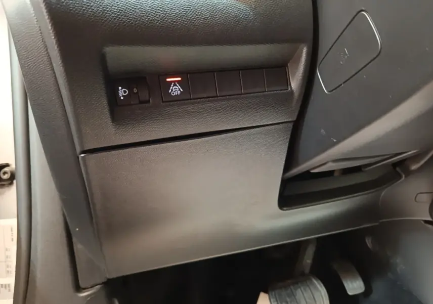 Vue intérieure côté gauche du tableau de bord gris foncé du Peugeot E-2008 électrique avec commandes d'assistance et pédales visibles.