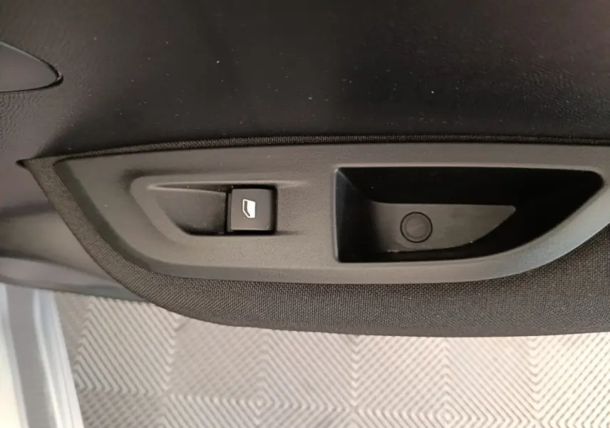 Détail du bouton d'ouverture de coffre sur le panneau intérieur noir d'un Peugeot E-2008 gris clair électrique.