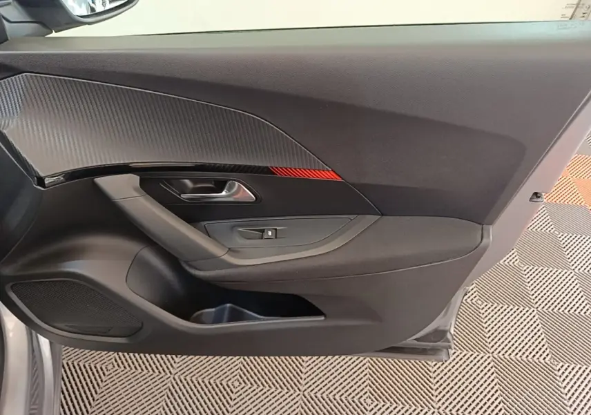 Intérieur côté gauche de la porte avant gris clair du Peugeot E-2008 électrique avec insert décoratif noir et rouge.