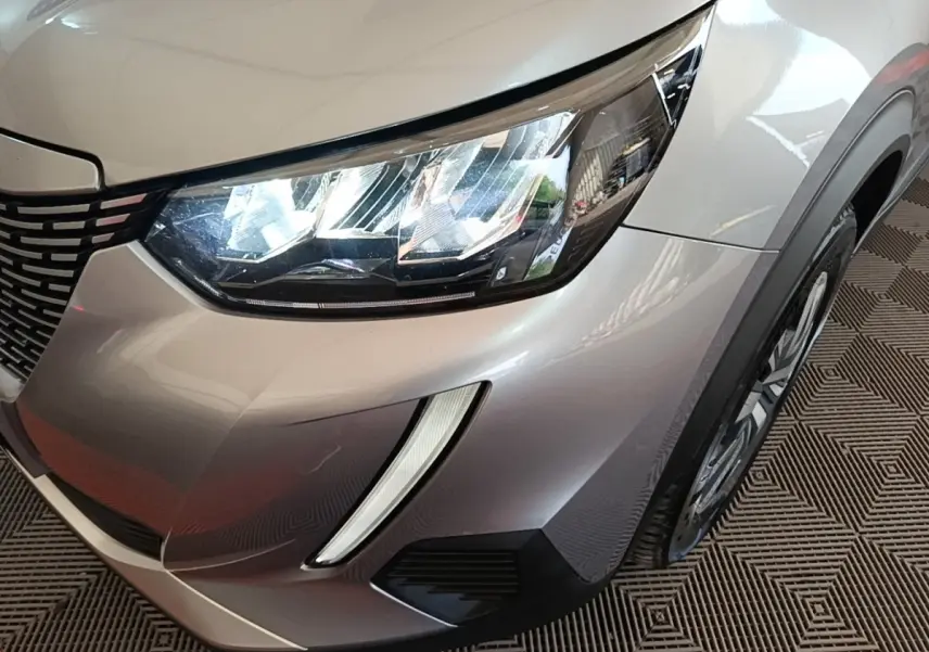Gros plan sur l'avant droit gris clair du Peugeot E-2008 électrique avec phares LED et calandre distinctive.