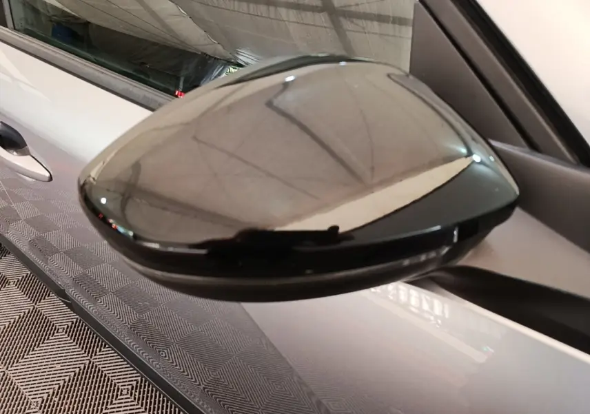 Rétroviseur noir brillant côté gauche d’un Peugeot E-2008 électrique gris clair, vue rapprochée en extérieur.