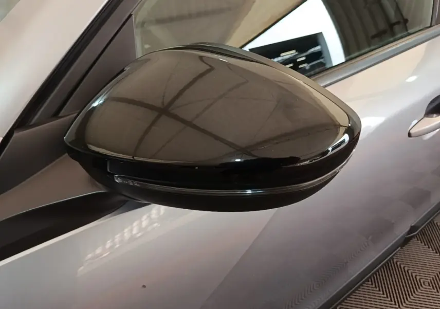 Rétroviseur noir en gros plan côté gauche d’un Peugeot E-2008 électrique gris clair, vue partielle du véhicule.