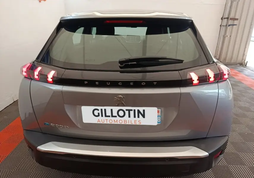 Vue arrière d'un Peugeot E-2008 électrique gris clair avec feux LED caractéristiques et logo central sur hayon.