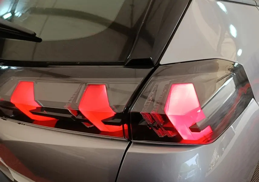 Gros plan sur les feux arrière rouges d’un Peugeot E-2008 électrique gris clair, vue côté droit arrière.