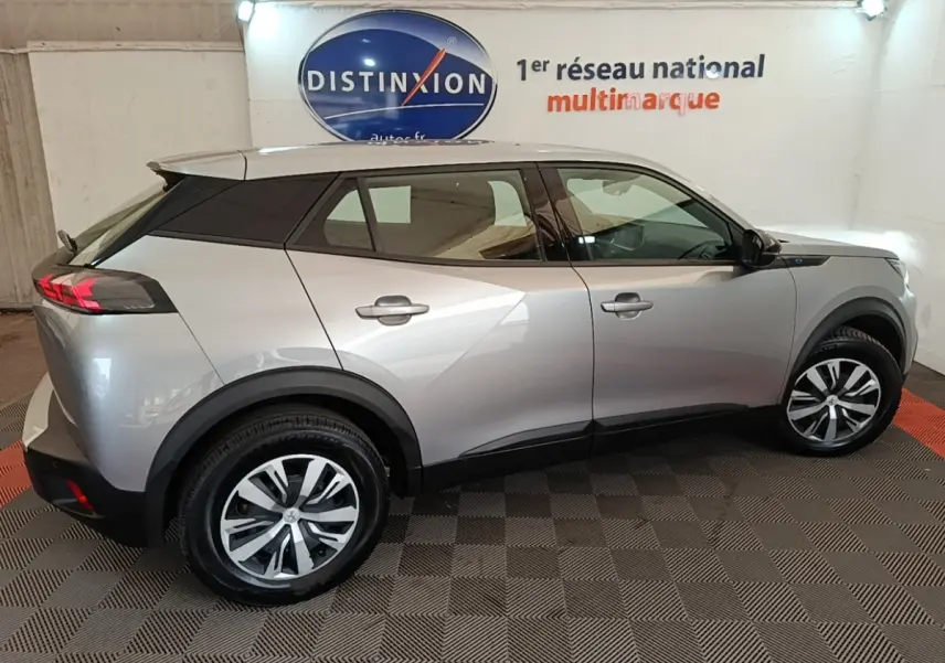 Vue de profil droit du Peugeot E-2008 électrique Active Pack gris clair, avec jantes distinctives et toit noir contrastant.