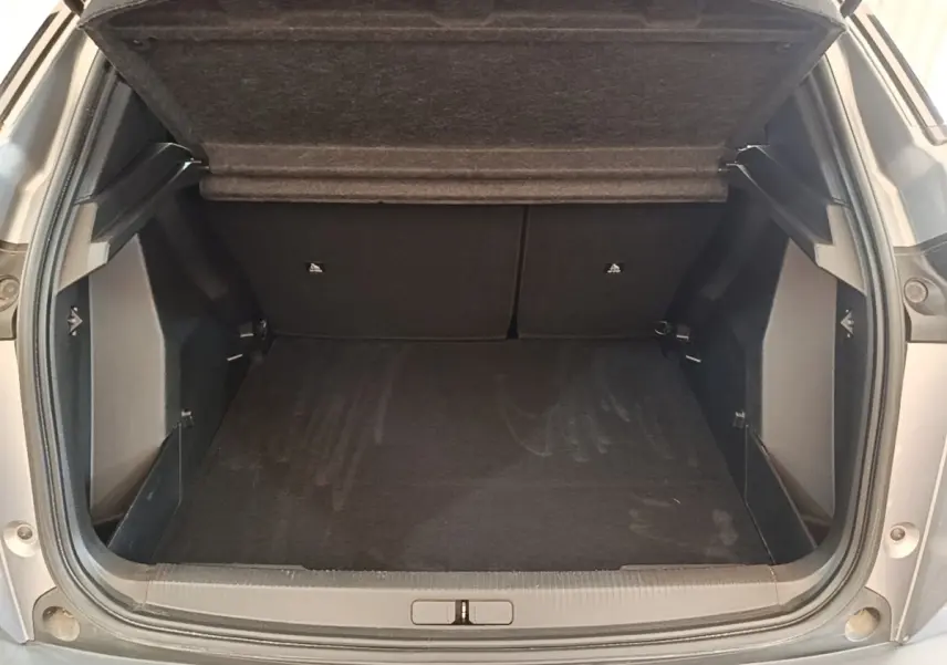 Coffre ouvert vu de l'arrière d'un Peugeot E-2008 électrique gris clair, montrant l'espace de chargement vide.