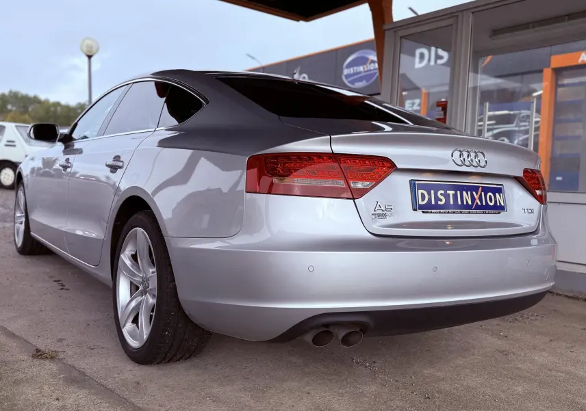 Vue 3/4 arrière gauche d'une Audi A5 gris métallisé avec feux arrière LED et double sortie d'échappement.