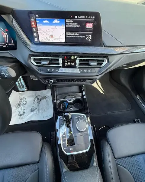 Vue intérieure centrée sur la console centrale et l'écran tactile de la BMW Série 1 118d Edition Sport gris foncé, avec volant cuir et commandes multifonctions.