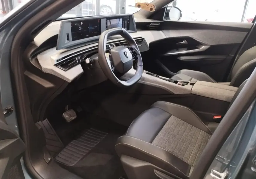 Vue intérieure côté conducteur du Peugeot 5008 2025 avec sellerie tissu gris et noir, volant compact et double écran HD flottant.