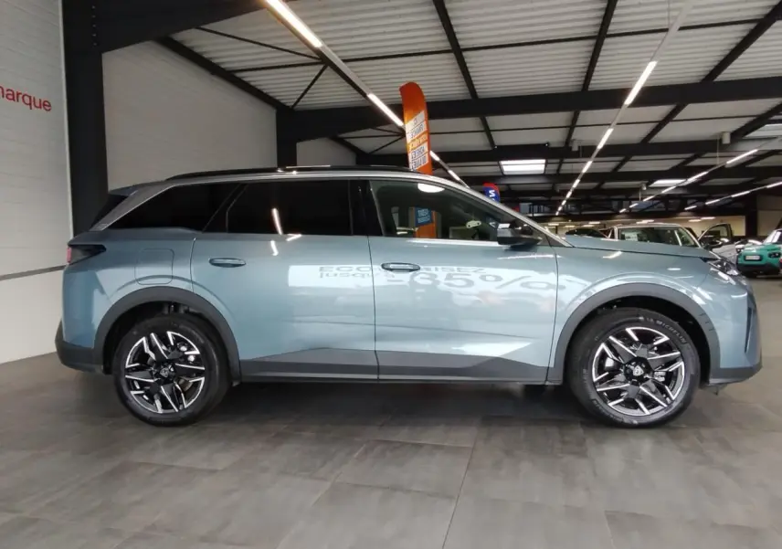 Vue de profil côté gauche d'un Peugeot 5008 bleu Ingaro métallisé avec jantes alliage 19'' noires diamantées en intérieur showroom.