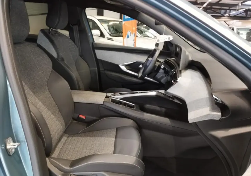 Intérieur avant droit du Peugeot 5008 bleu Ingaro 2025, sièges tissu et cuir, planche de bord avec décor tissu clair.