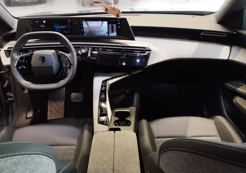 Vue intérieure avant du Peugeot 5008 2025 avec tableau de bord noir et tissu gris, volant compact et double écran HD flottant.