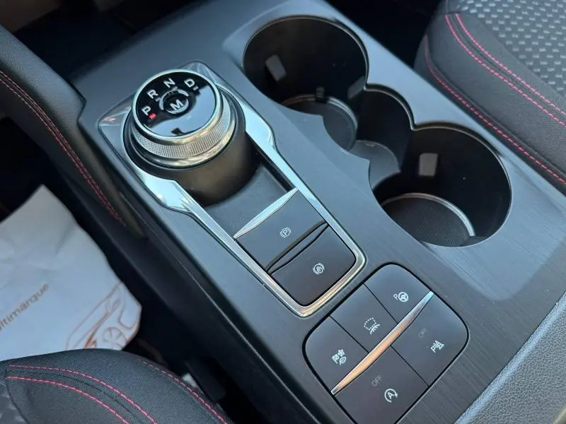 Vue rapprochée de la console centrale noire avec molette de sélection de vitesse et surpiqûres rouges sur siège Ford Kuga 2024.