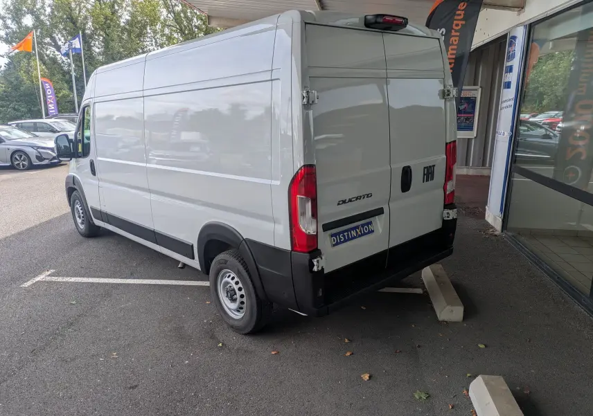 Fiat Ducato Fourgon blanc en vue 3/4 arrière droit, stationné devant un bâtiment avec portes arrière fermées.
