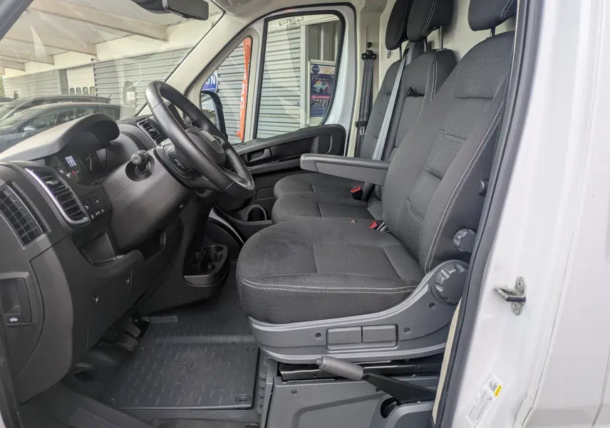 Vue intérieure côté conducteur du Fiat Ducato Fourgon blanc 2025, montrant les sièges noirs et le tableau de bord.