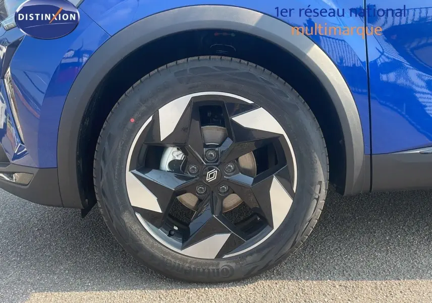 Gros plan sur la roue avant gauche d'un Renault Captur bleu Iron Metal avec jante noire et argentée au design étoile.