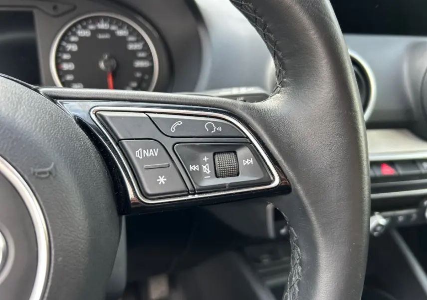 Gros plan sur les commandes gauche du volant cuir noir de l'Audi Q2 35 TFSI 2023 avec tableau de bord en arrière-plan.