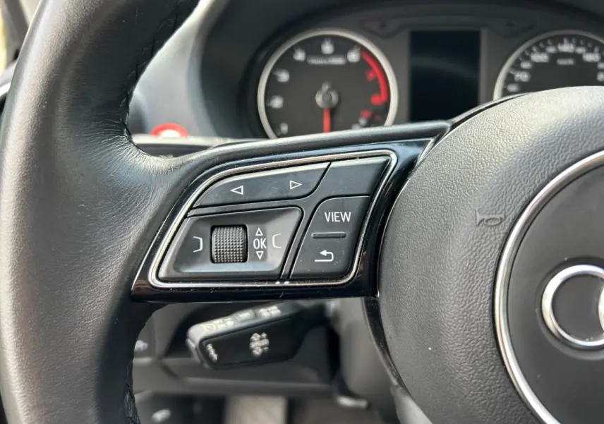 Gros plan sur les commandes du volant côté gauche de l'Audi Q2 35 TFSI 150 S Line 2023 avec cuir noir.