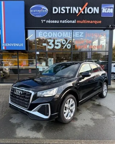Audi Q2 noir vue 3/4 avant droit, garée devant une concession Distinxion avec reflets sur la carrosserie.