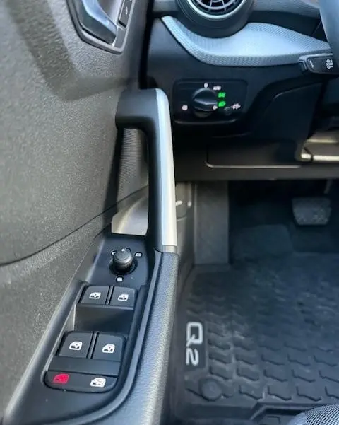 Gros plan sur la commande des vitres et rétroviseurs côté gauche d’un Audi Q2 noir, avec tapis de sol marqué Q2 visible.