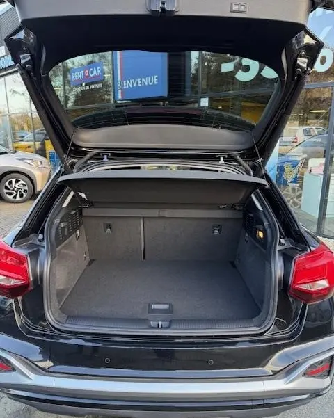 Coffre ouvert vu de l’arrière d’un Audi Q2 noir 2023, montrant l’espace de chargement et la tablette de séparation.
