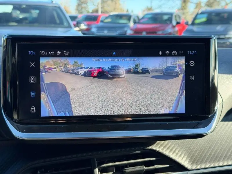 Écran tactile intérieur du Peugeot 2008 2024 affichant la caméra de recul avec vue arrière sur parking ensoleillé.