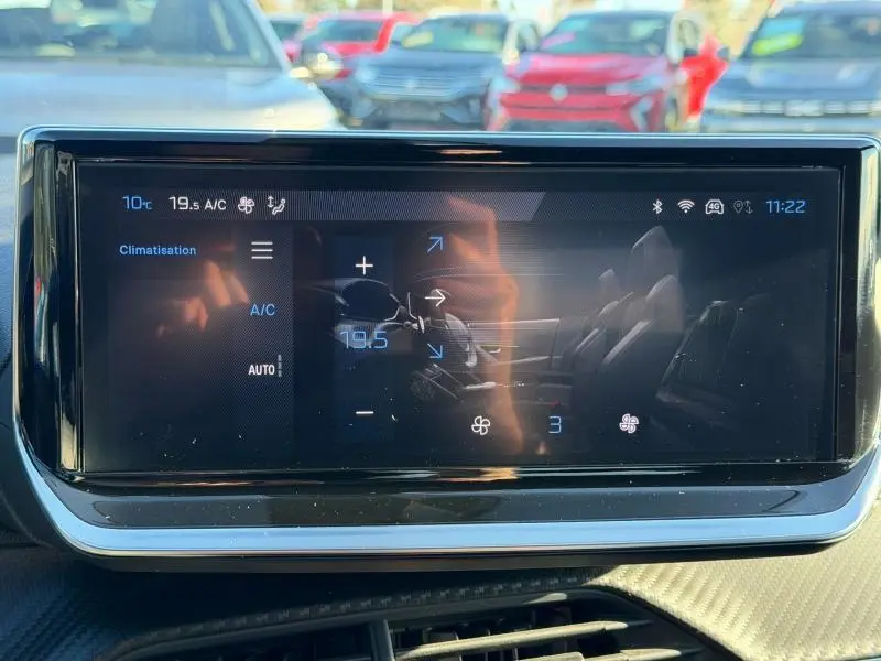 Écran tactile central affichant la climatisation du Peugeot 2008 gris, vue intérieure frontale avec reflets extérieurs.