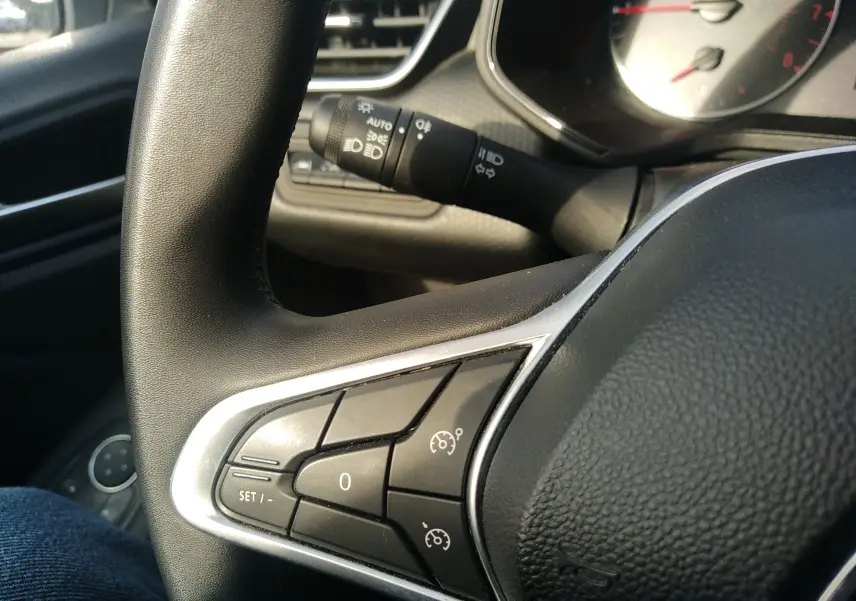 Gros plan sur les commandes au volant côté gauche de la Renault Clio V 2023, finition tissu noir, intérieur gris.