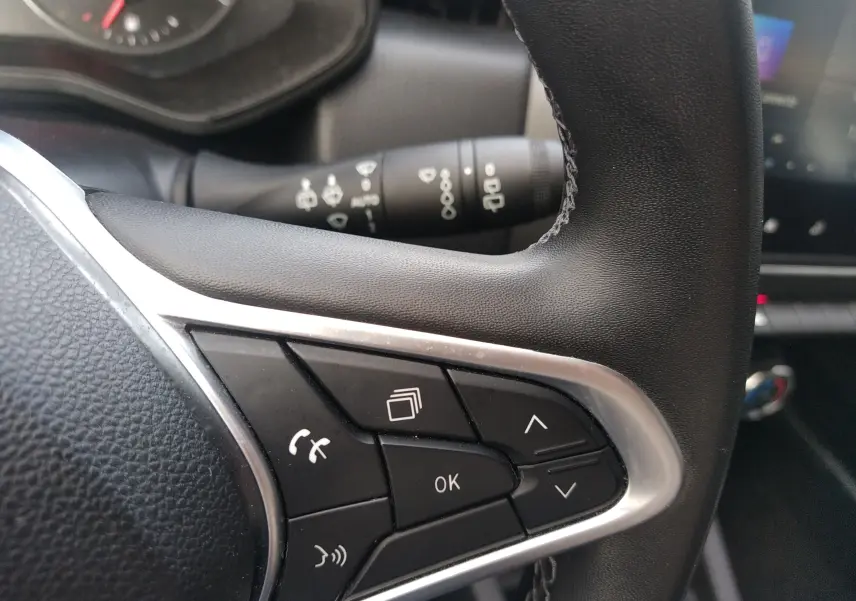 Gros plan sur les commandes multifonctions noires du volant en cuir d’une Renault Clio V gris, intérieur moderne.