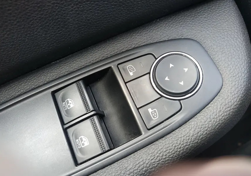 Gros plan sur les commandes de réglage des vitres et des rétroviseurs électriques côté conducteur d'une Renault Clio V gris 2023.