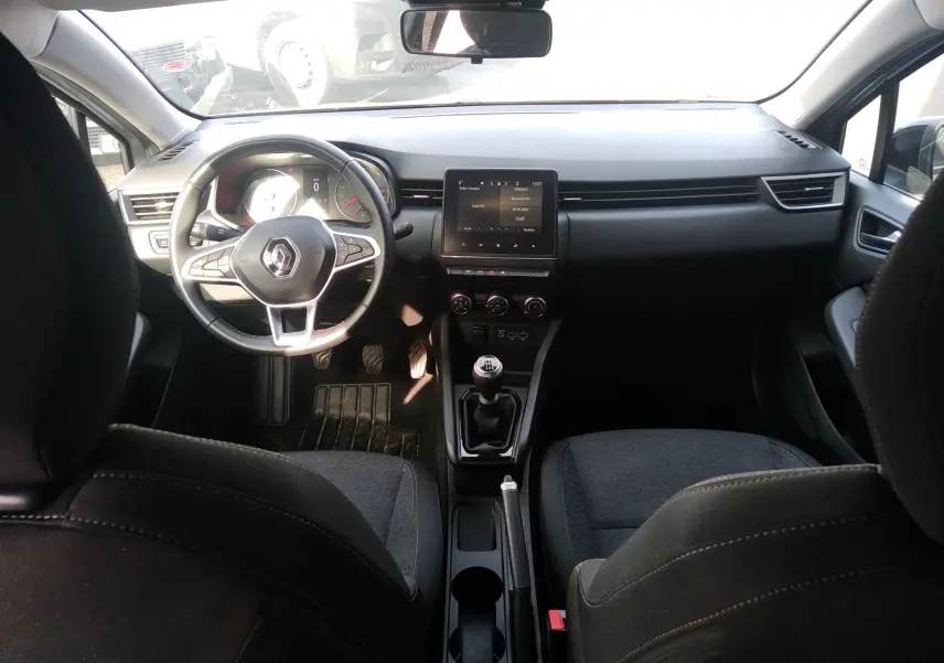 Vue intérieure avant de la Renault Clio V gris, volant multifonctions, écran tactile central et boîte manuelle visible.