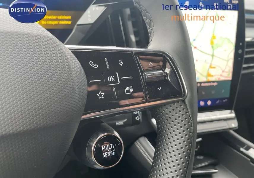 Gros plan sur le volant perforé et les commandes multifonctions du Renault Austral 1.2 E-Tech gris métal, avec écran tactile en arrière-plan.
