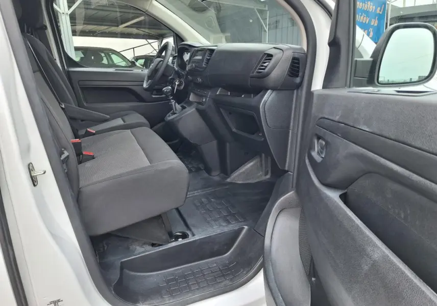 Vue intérieure côté conducteur de l'Opel Vivaro blanc 2025, montrant les sièges avant et le tableau de bord noir.
