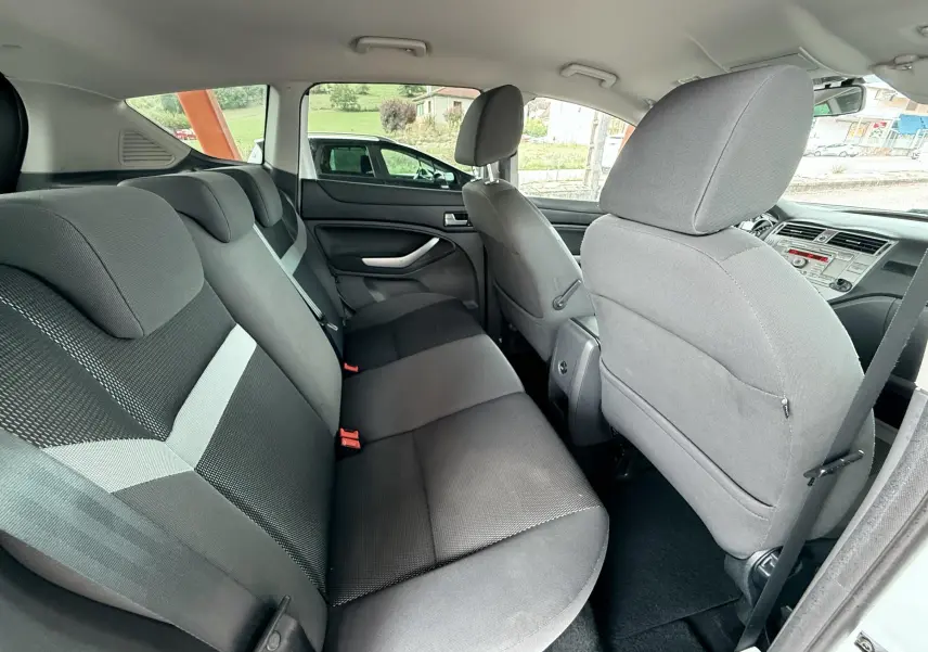 Vue intérieure arrière du Ford Kuga 2012 montrant les sièges en tissu gris et noir avec porte ouverte côté droit.