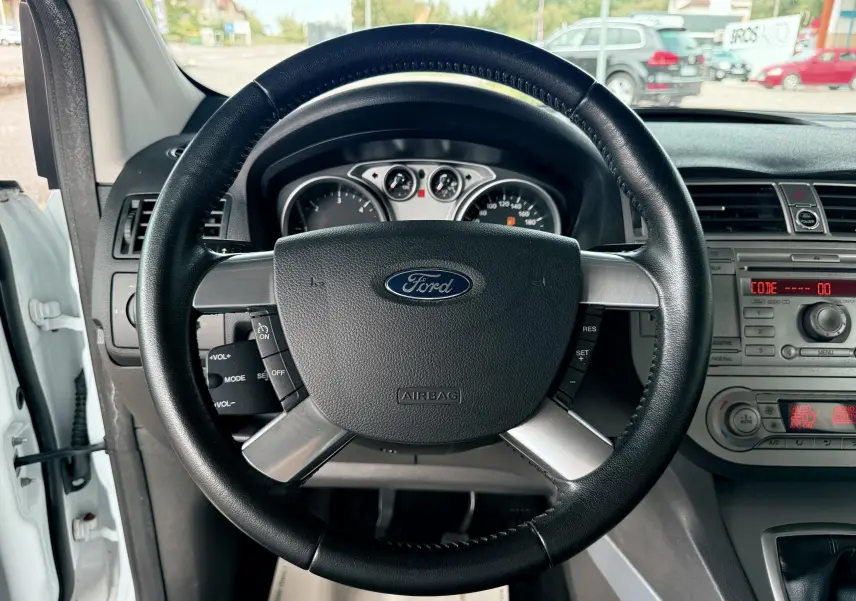 Vue intérieure centrée sur le volant noir du Ford Kuga blanc 2012 avec tableau de bord et commandes visibles.