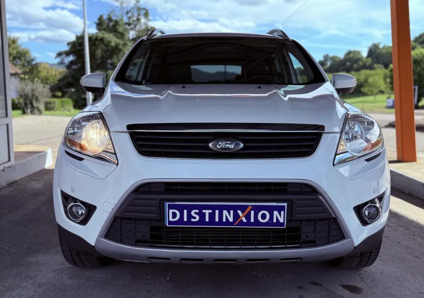 Vue frontale d'un Ford Kuga blanc de 2012 avec phares allumés et plaque Distinxion visible.