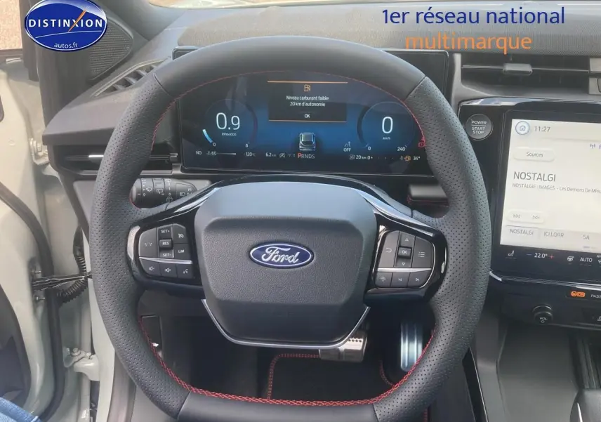 Vue frontale du volant perforé avec surpiqûres rouges du Ford Puma gris cactus, tableau de bord numérique et écran tactile visible.