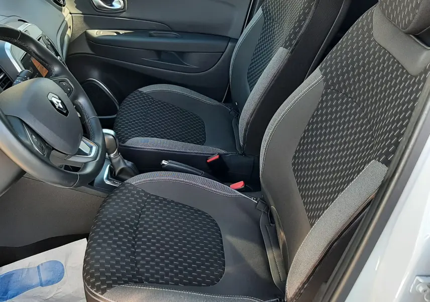 Intérieur côté conducteur du Renault Captur blanc nacré, sièges tissu gris noir avec motifs géométriques visibles.