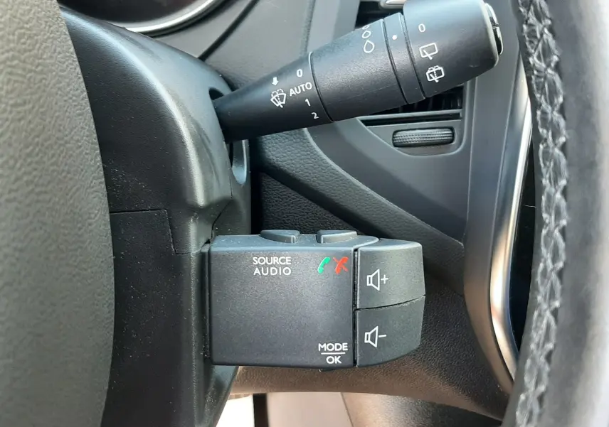 Gros plan sur la commande audio au volant côté gauche du Renault Captur blanc nacré avec toit noir, intérieur gris noir.