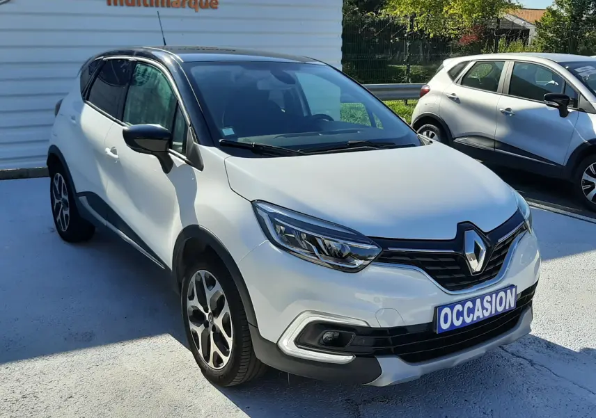 Renault Captur blanc nacré avec toit noir, vu en 3/4 avant droit sur parking extérieur lumineux.