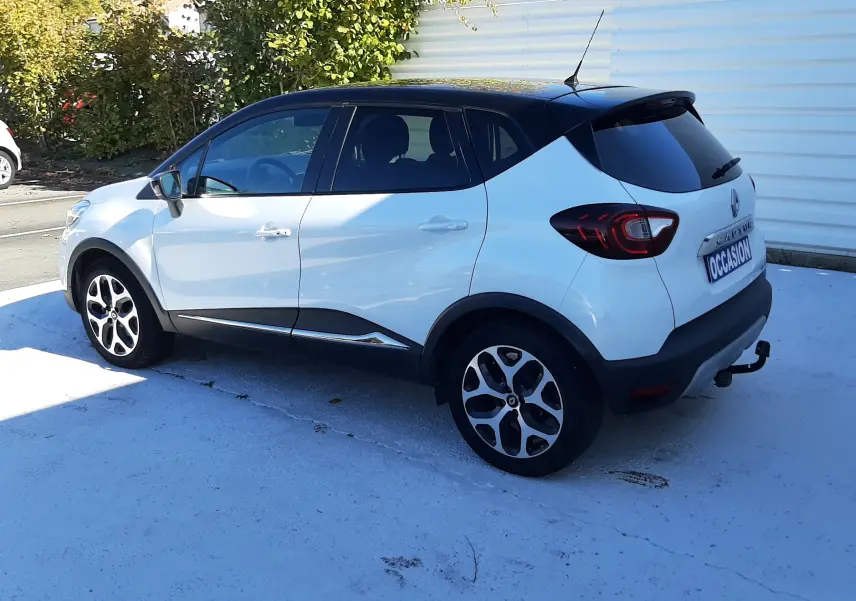 Renault Captur blanc nacré avec toit noir en vue 3/4 arrière côté droit, roues alliage et attelage visibles.