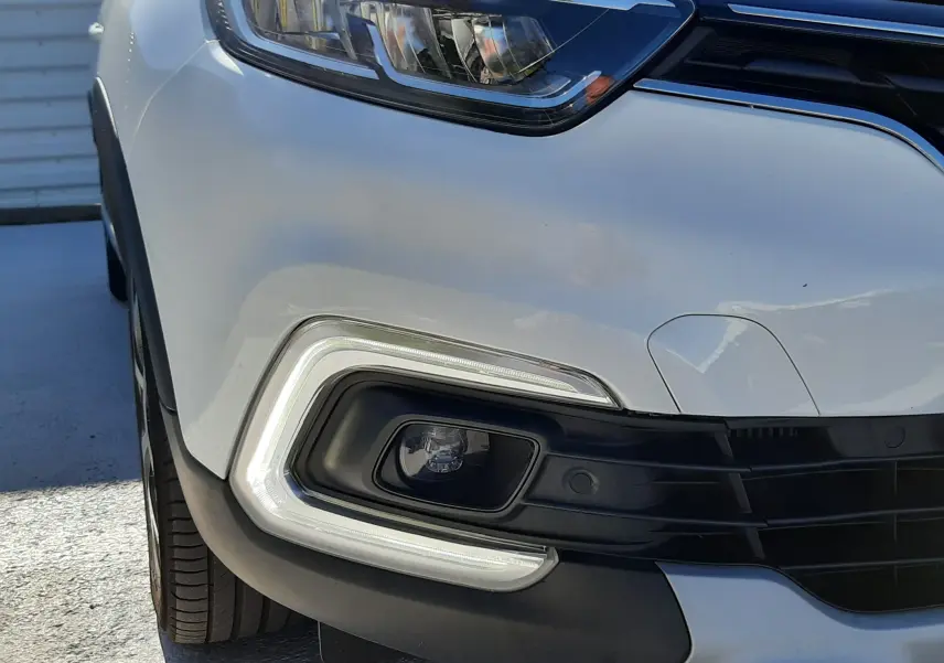 Gros plan sur le phare avant gauche et le pare-chocs blanc nacré du Renault Captur 2019 avec éclairage LED distinctif.