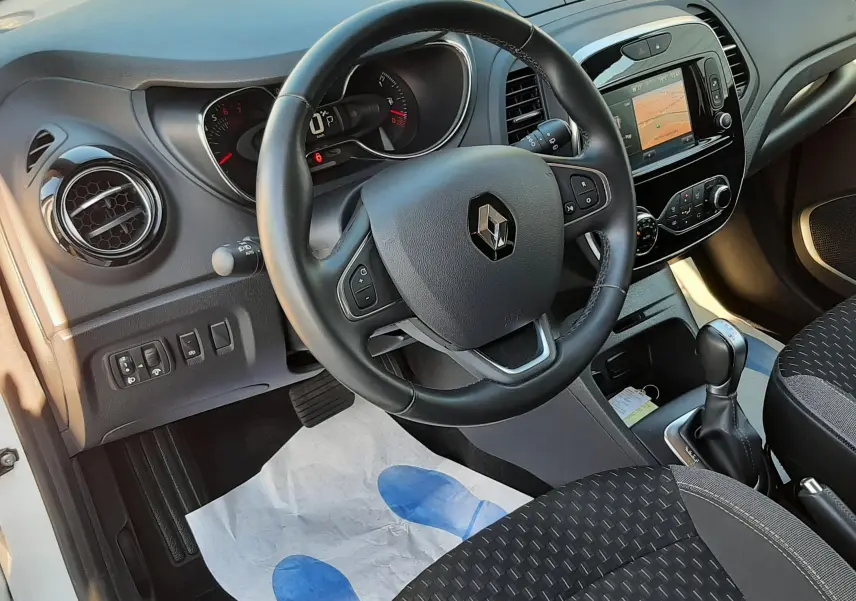 Vue intérieure côté conducteur du Renault Captur 2019, volant cuir, tableau de bord noir et sièges tissu gris-noir.