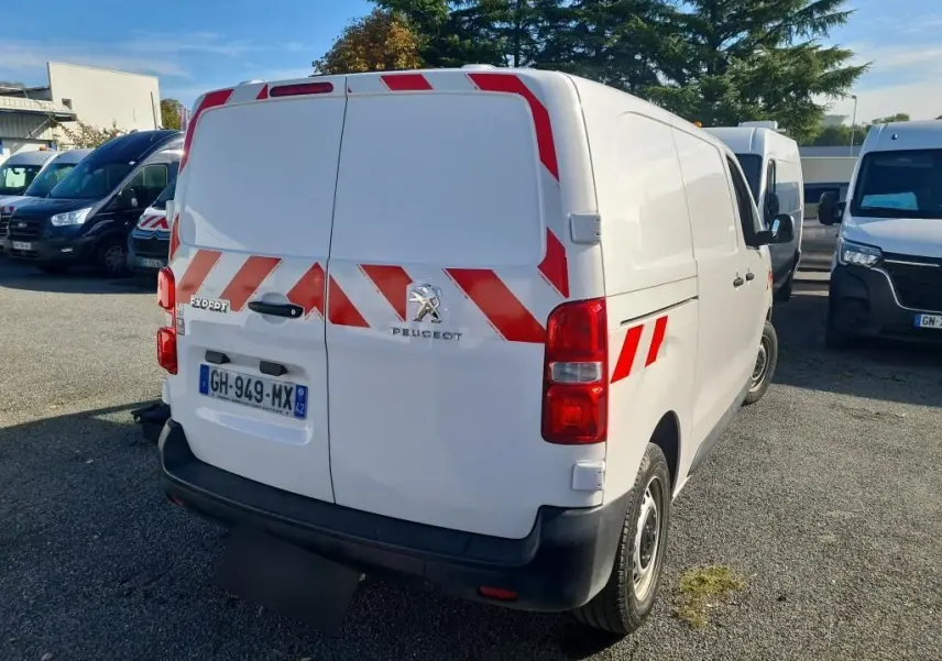 Vue 3/4 arrière d'un Peugeot Expert Fourgon blanc 2022 avec bandes réfléchissantes rouges et gyrophare.