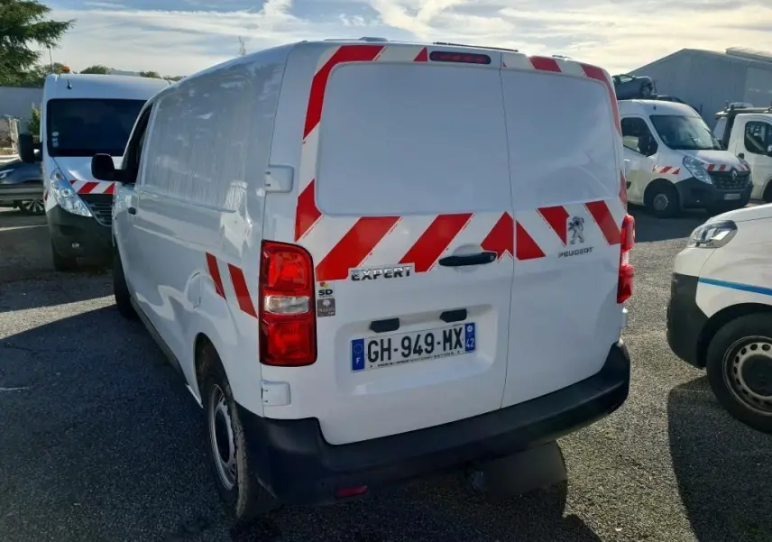 Vue arrière droite d'un Peugeot Expert Fourgon blanc 2022 avec bandes rouges réfléchissantes et gyrophare au toit.