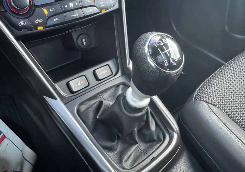 Gros plan sur le levier de vitesses manuel noir et argenté du Suzuki S-Cross blanc 2023 avec commandes de sièges chauffants visibles.