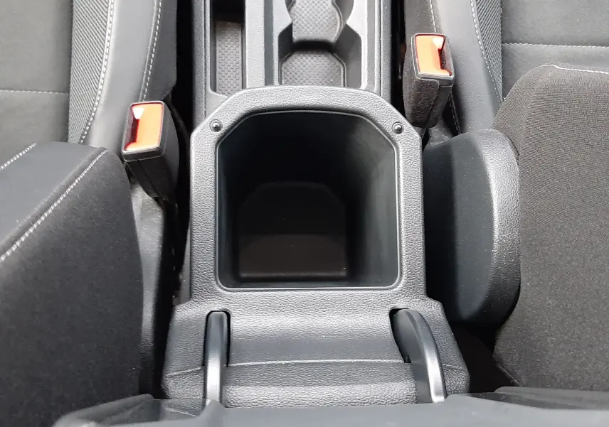 Vue plongeante sur la console centrale noire du Volkswagen T-Roc 2023, avec porte-gobelets et ceintures rouges visibles.